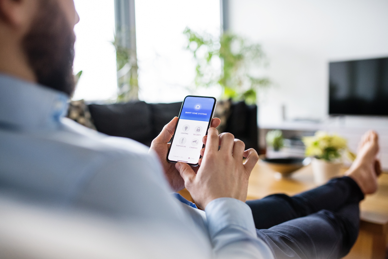 A man holding a smartphone with smart home screen of home automation controls 