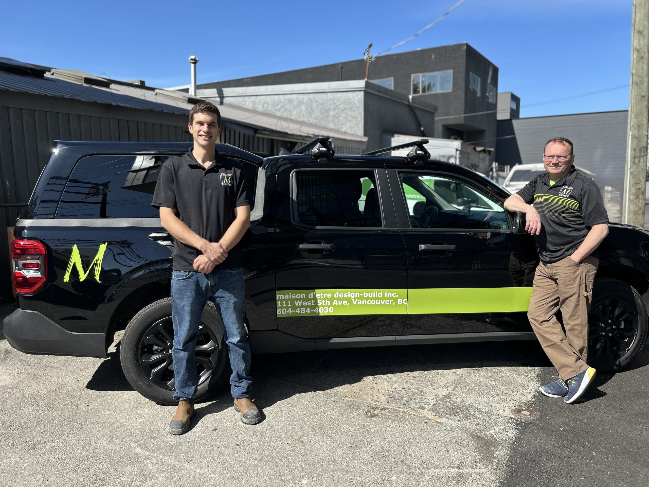 Two team members standing beside a black maison d’etre vehicle parked outside.