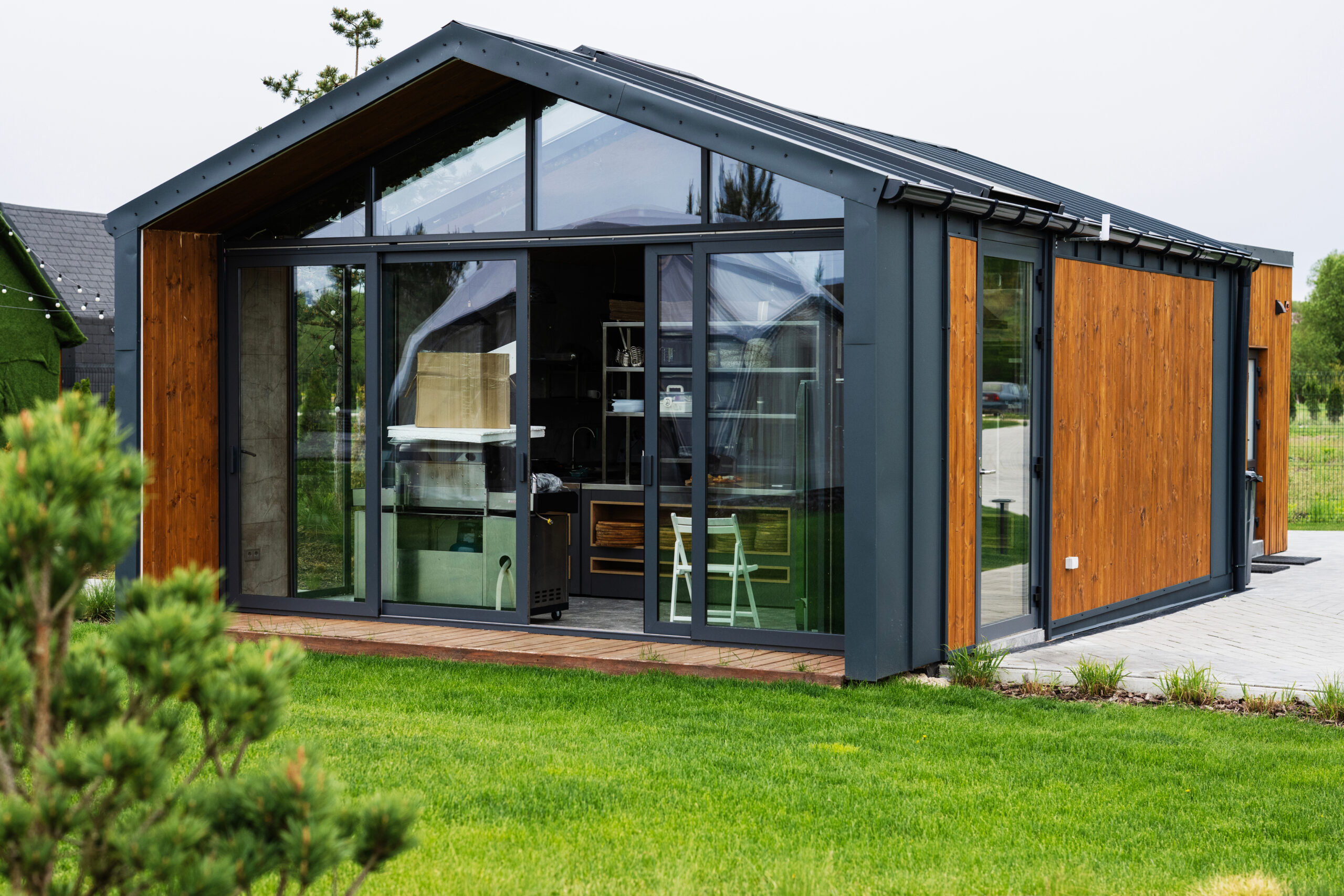 Compact prefab modern house with glass walls and landscaped green outdoor surroundings