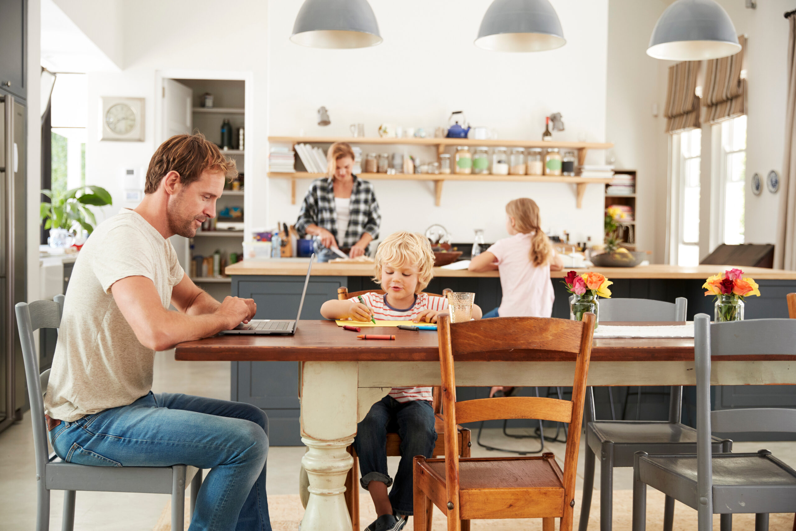 A family working and playing at a dining table with the open kitchen visible behind them