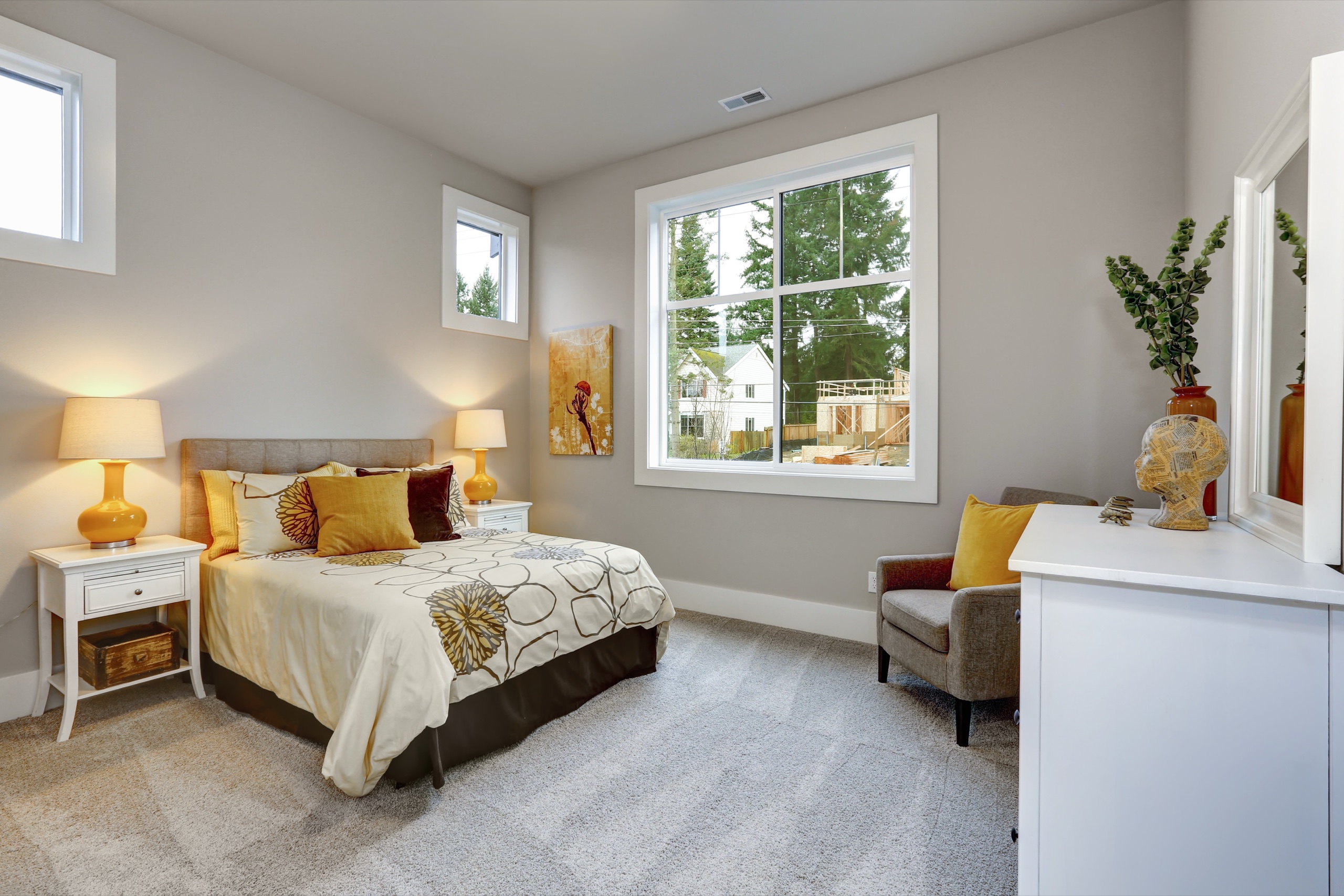 Guest bedroom with grey walls, yellow accent pillows, bedside lamps, and a large window