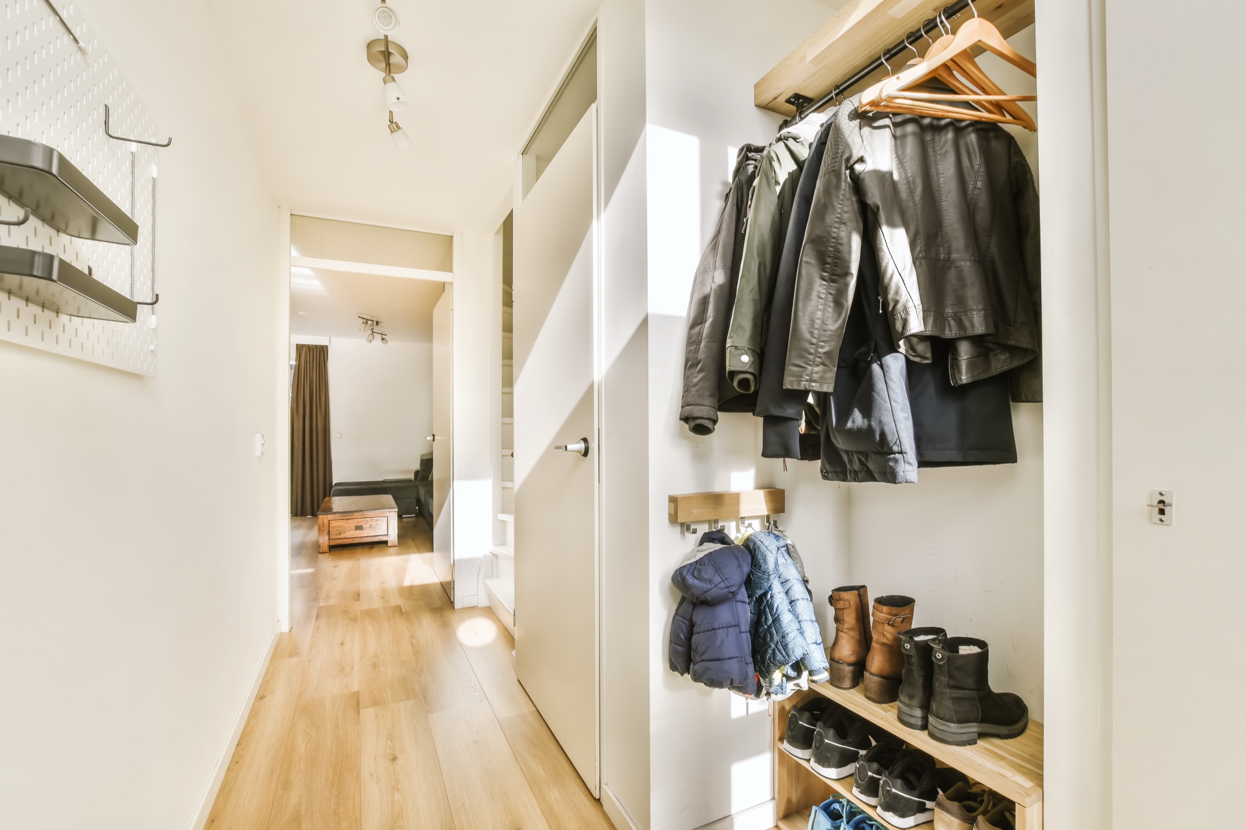 Entryway closet with hanging coats, a wooden shoe rack, and light wood flooring leading down the hall