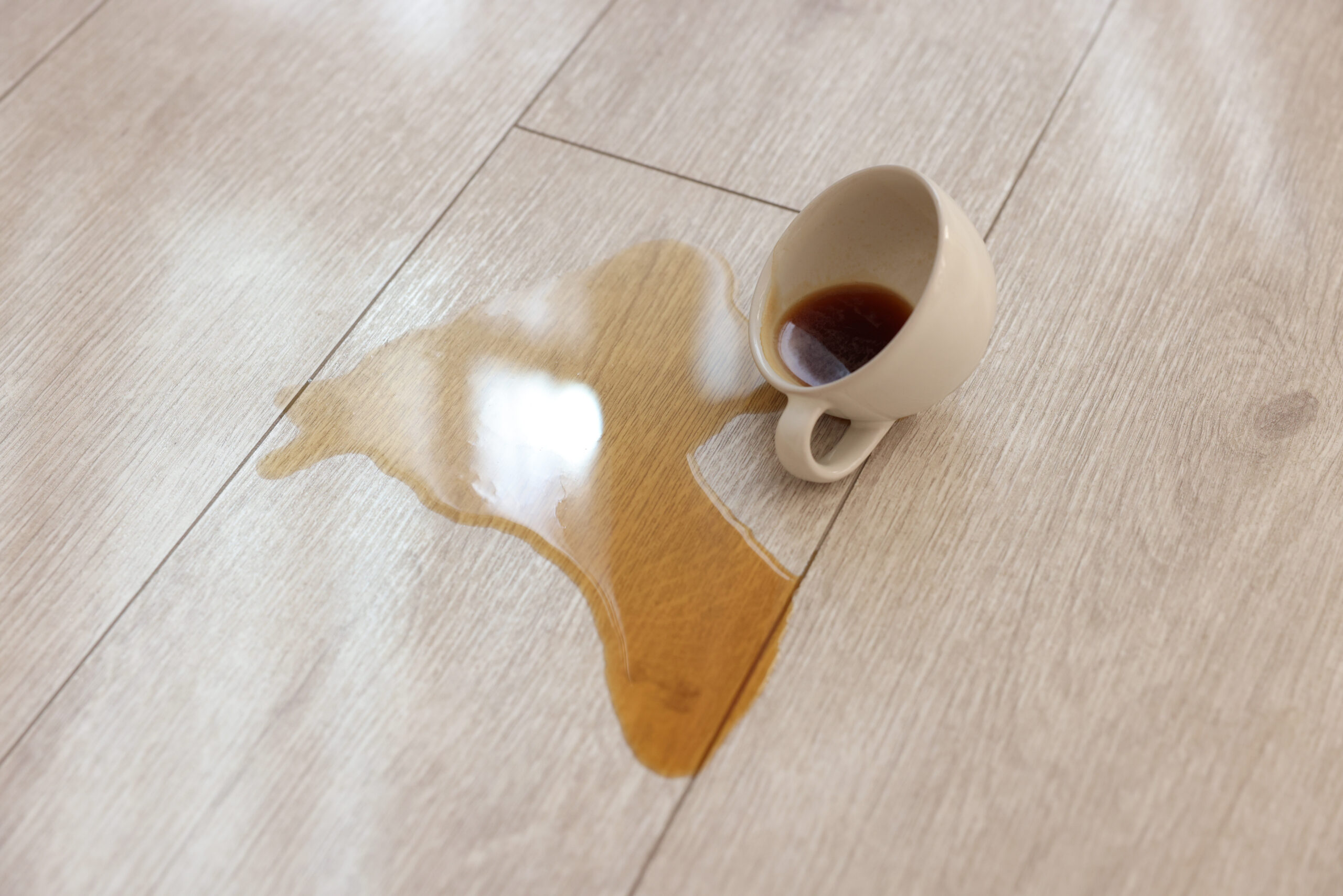 A tipped cup spilling a drink across a wood-look floor